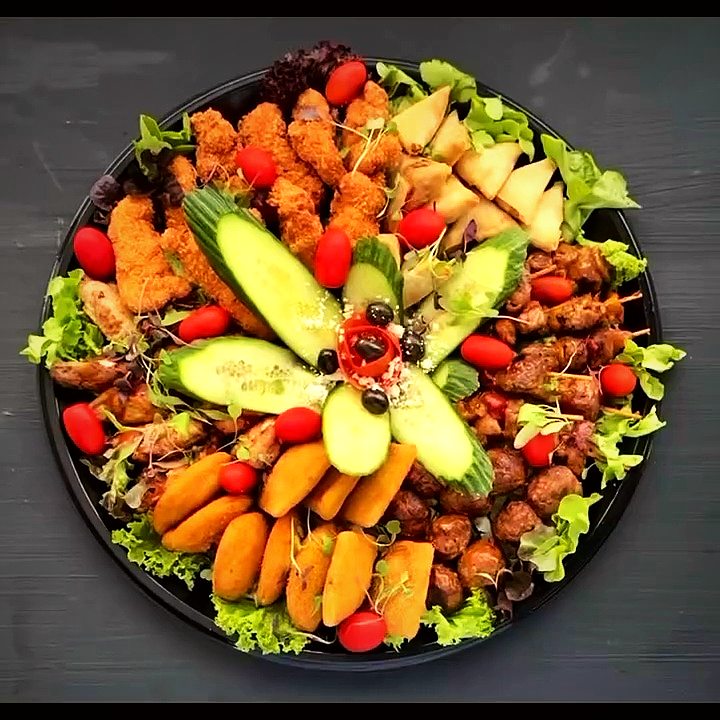 A round platter of samoosas, spring rolls and skewers garnished with cucumber