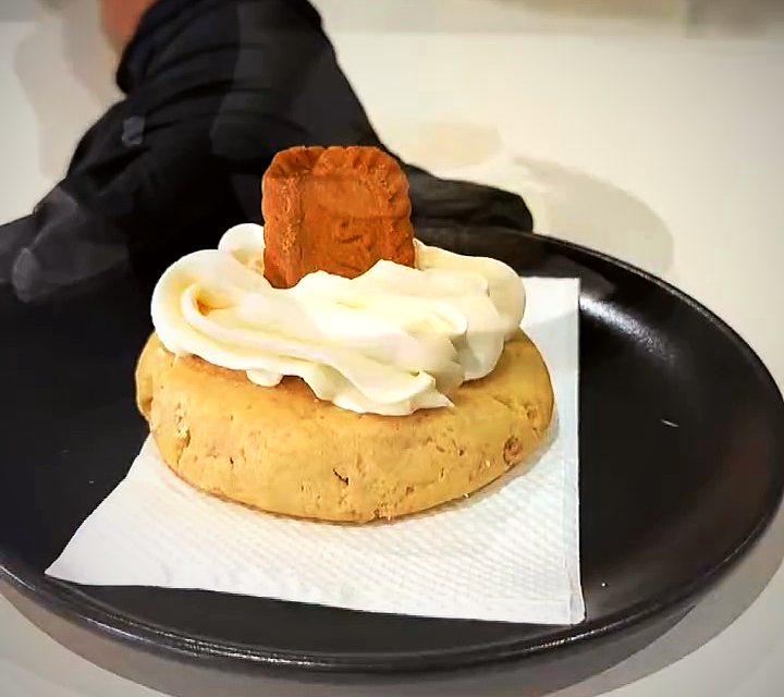 A Biscoff cookie topped with cream and a Lotus biscuit